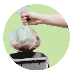 A hand holding a full bag of food waste over a kitchen caddy.