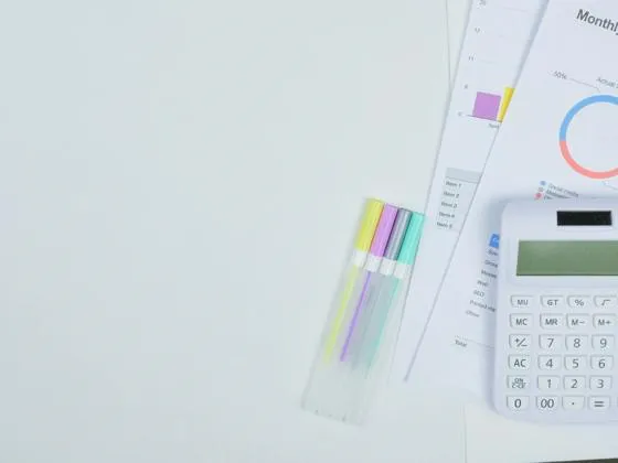 A set of pens and a calculator on top of some monthly budget reports.