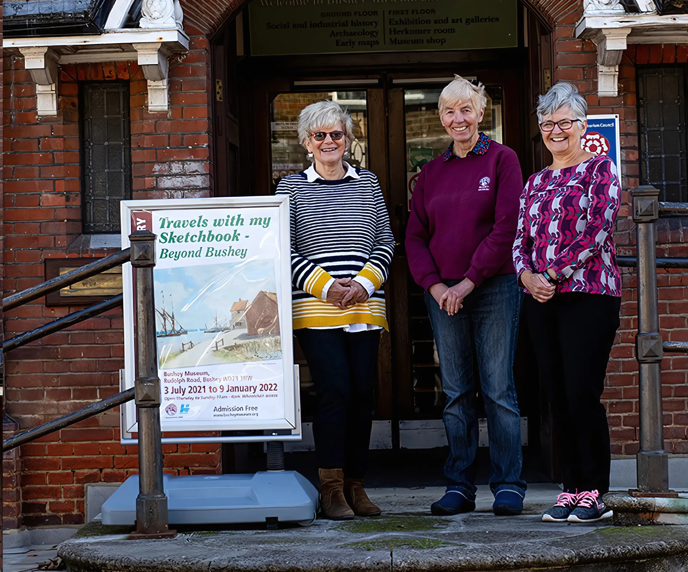Three Bushey Museum Volunteers face the camera smiling outside of the museum