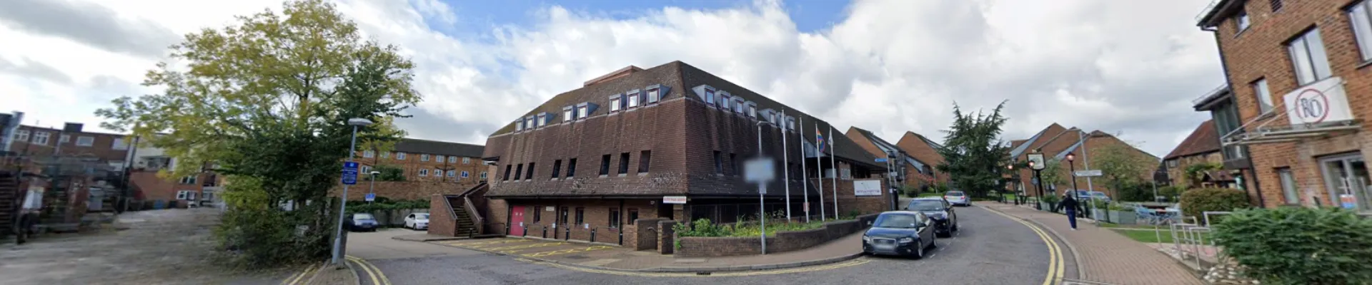 The exterior building of Wyllyotts Centre in Potters Bar with cars parked alongside the road.
