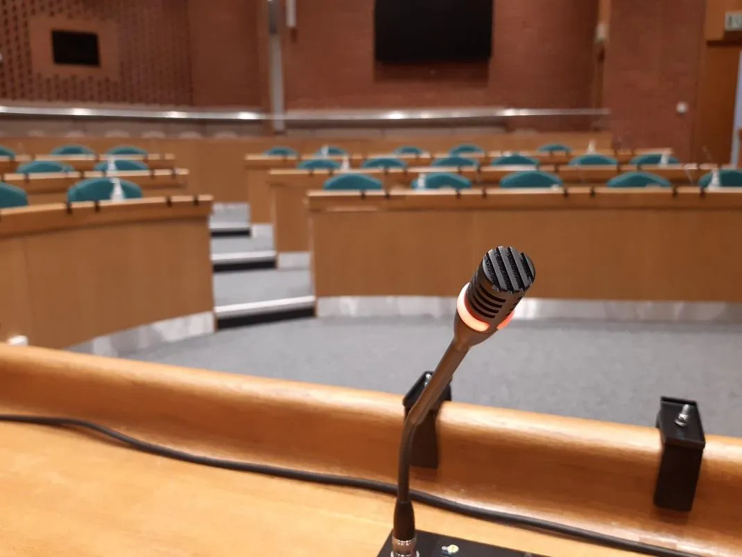 A view of the committee room from a member's point of view. Microphone in foreground, pointed at viewer. Seats on other side.